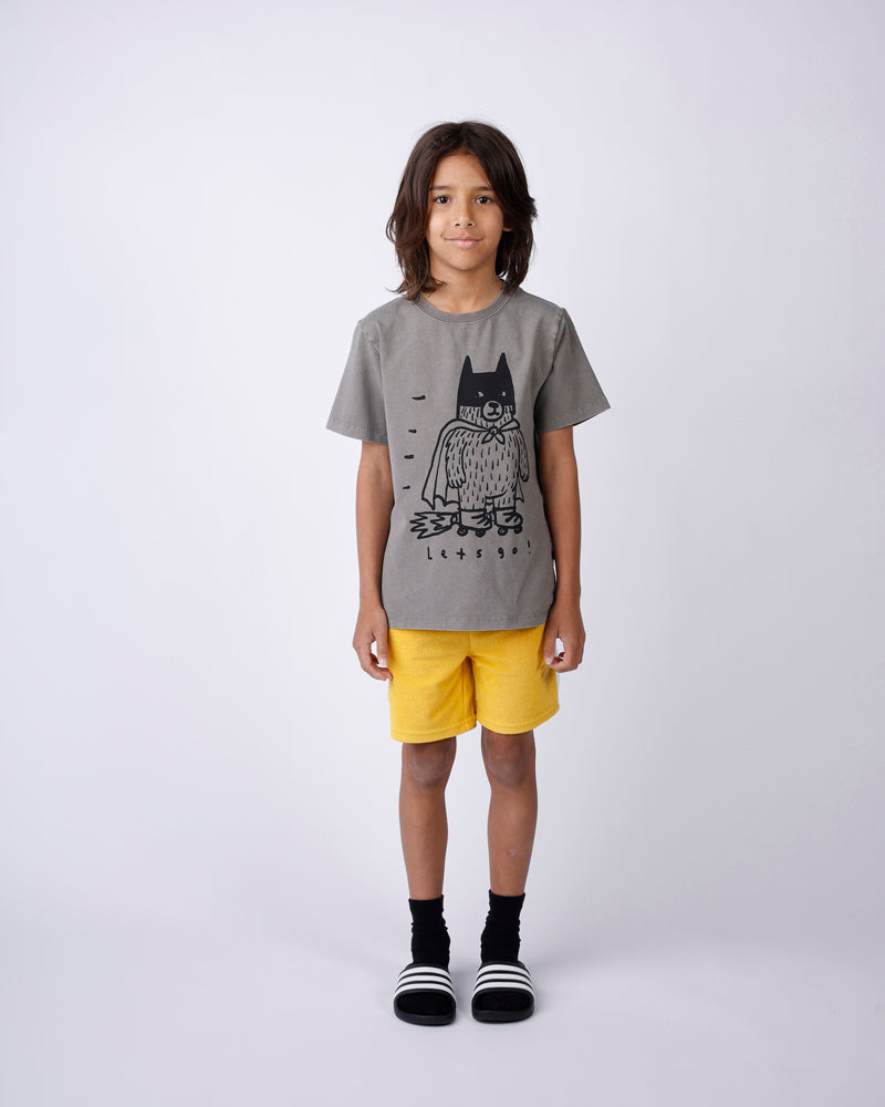 Child wearing a gray t-shirt with a graphic design and yellow shorts on a white background