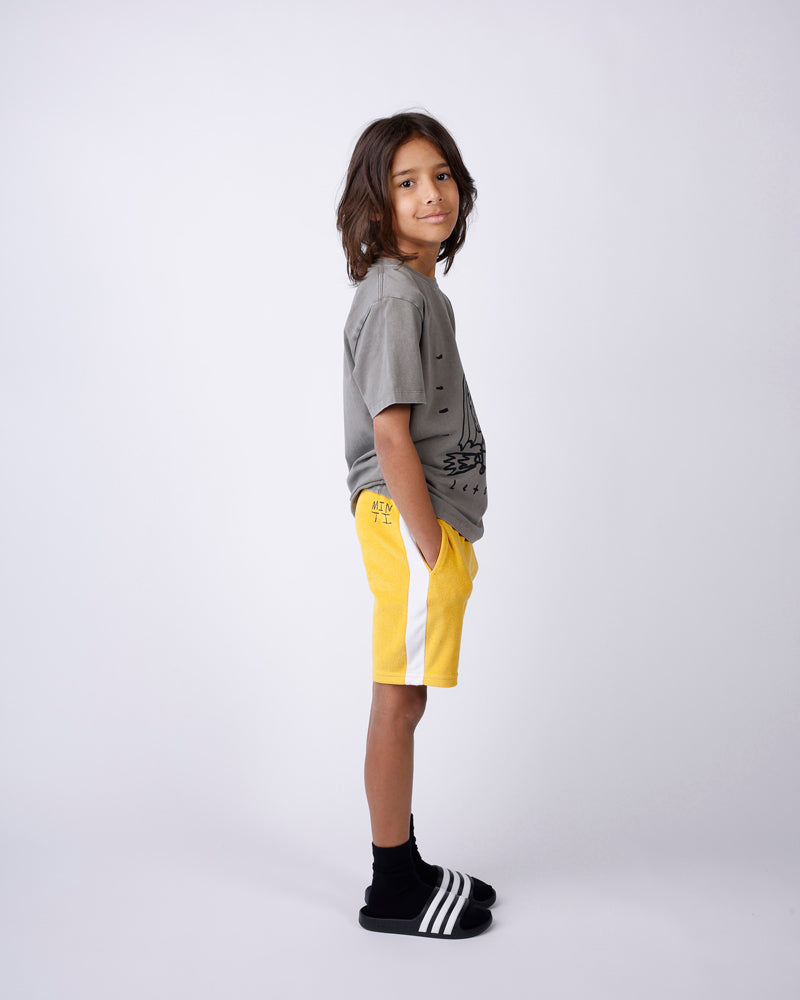 Child wearing a gray shirt and yellow shorts on a white background