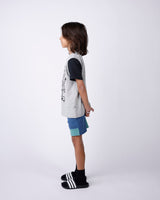 Child wearing a gray shirt with black sleeves and blue shorts on a white background