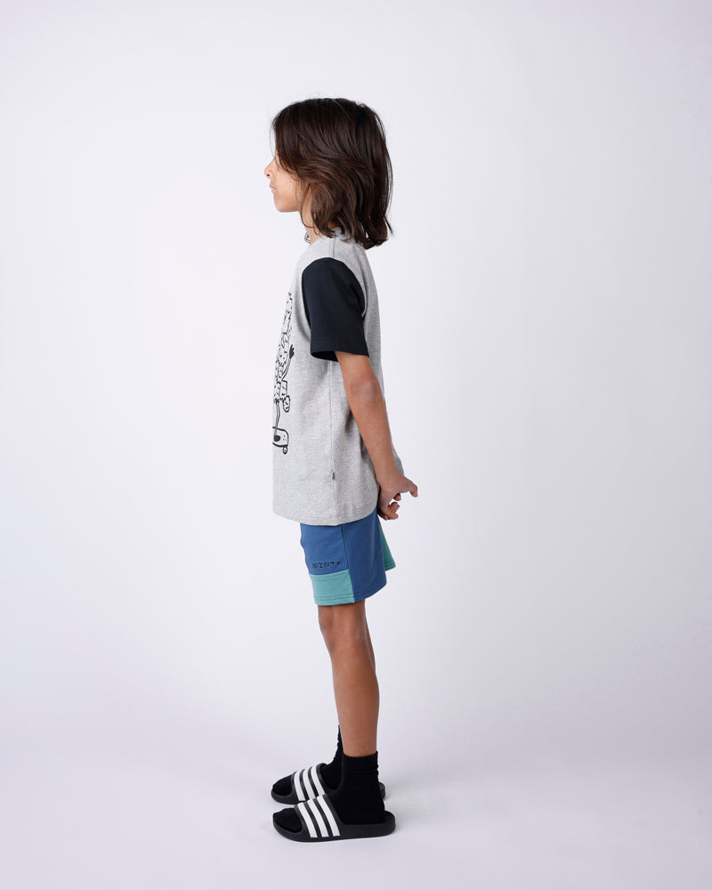Child wearing a gray shirt with black sleeves and blue shorts on a white background