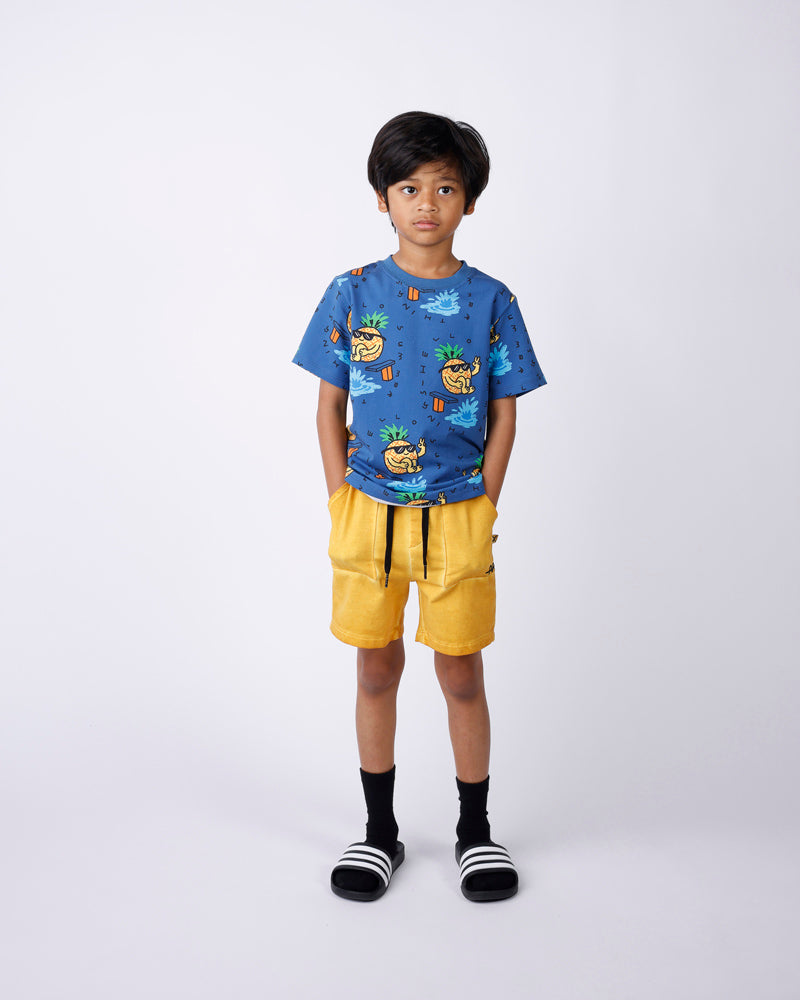 Child wearing a blue t-shirt with a colorful design and yellow shorts on a white background