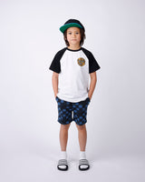 Child wearing a black and white t-shirt, blue checkered shorts, and a green cap on a white background