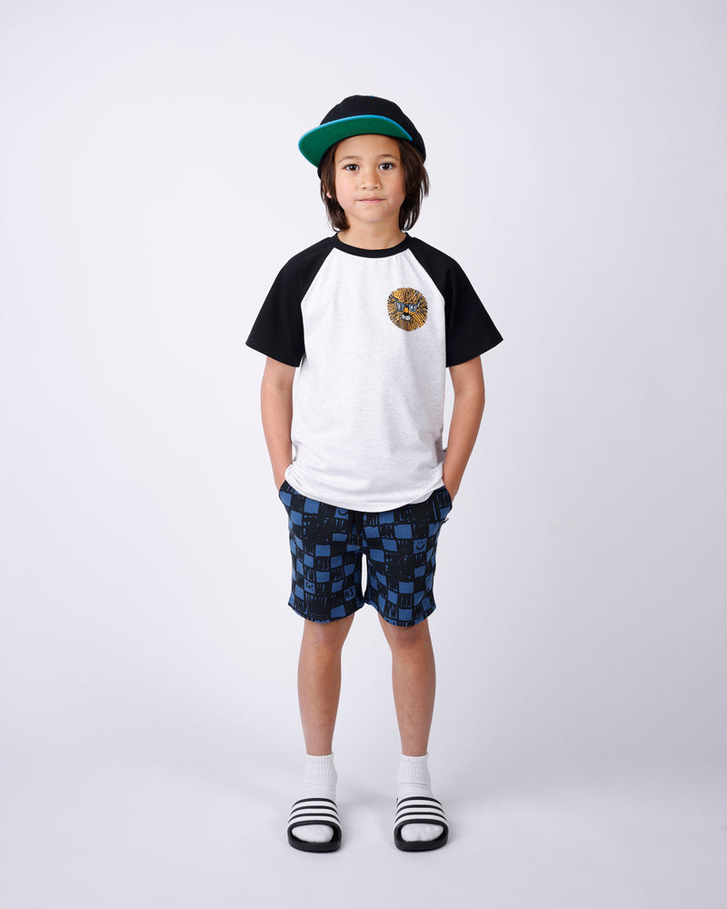Child wearing a black and white t-shirt, blue checkered shorts, and a green cap on a white background