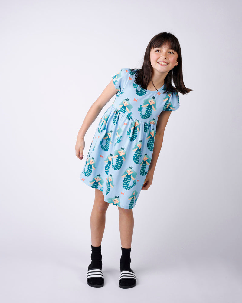 Young girl wearing a light blue dress with mermaid pattern on a white background