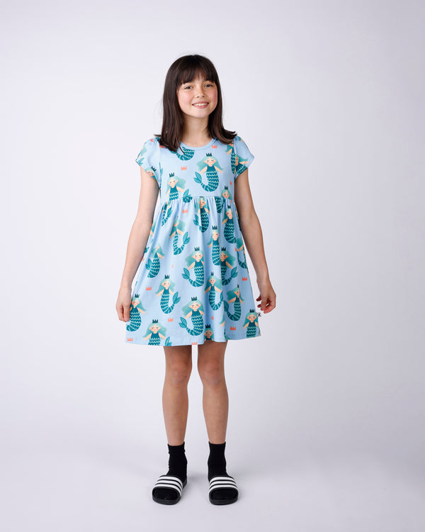 Young girl wearing a light blue dress with mermaid pattern on a white background