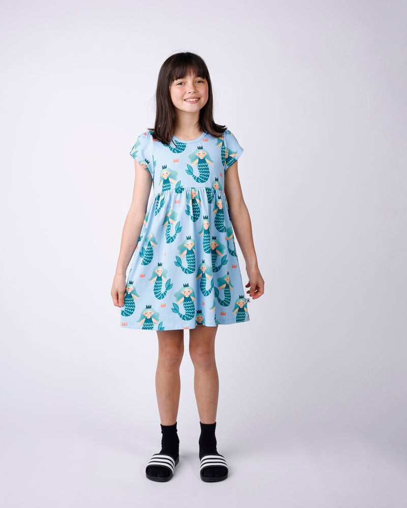 Young girl wearing a light blue dress with mermaid pattern on a white background
