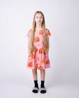 Young girl wearing a pink dress with orange watermelon pattern on a white background
