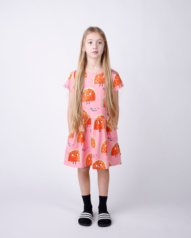 Young girl wearing a pink dress with orange watermelon pattern on a white background