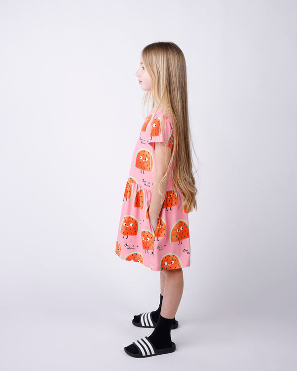 Young girl wearing a pink dress with orange patterns on a white background