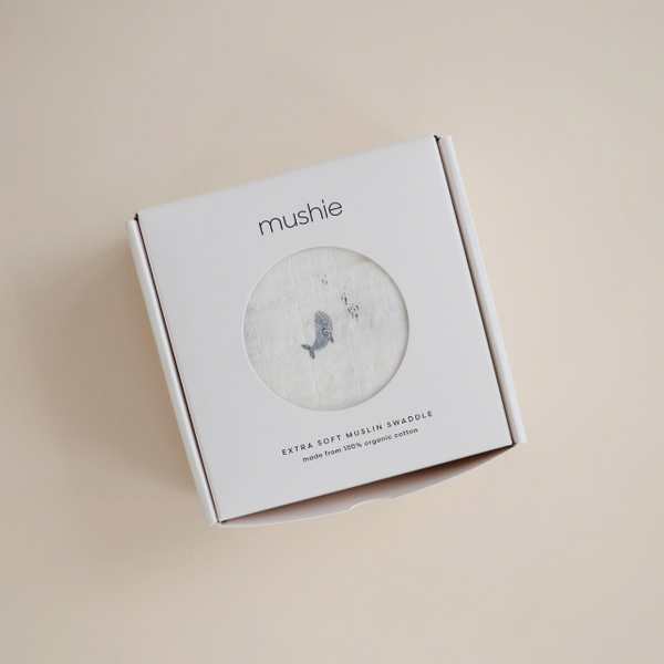 Whale muslin in Mushie product packaging on a beige background