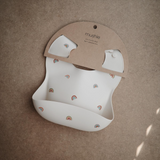 Beige bib with rainbow pattern and brown packaging on a brown background