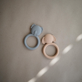 Two silicone teething rings, one grey koala and one natural dog on a beige background