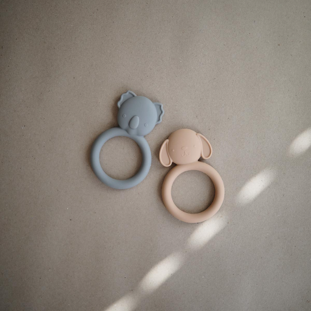 Two silicone teething rings, one grey koala and one natural dog on a beige background