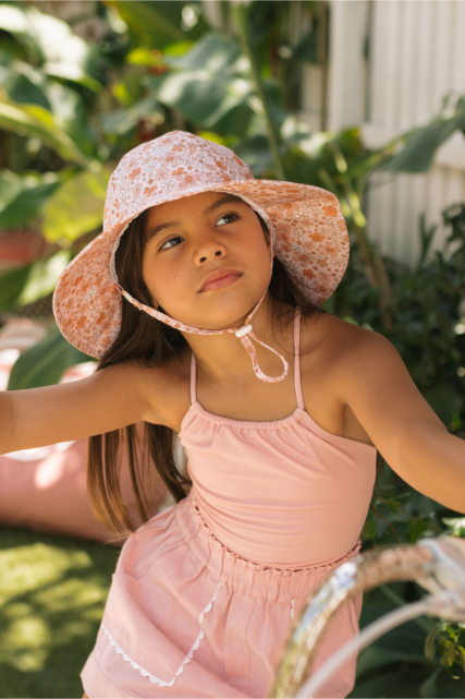 Young girl wearing a floral sun hat and pink dress outdoors.