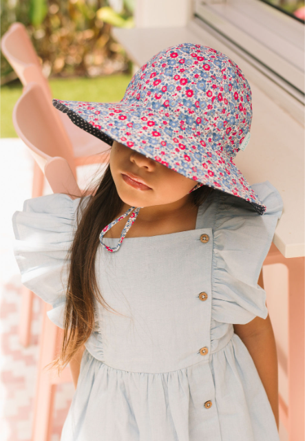 Young girl wearing a floral sun hat and light blue dress outdoors.