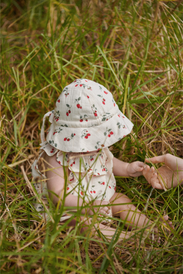 Baby in a strawberry sun hat sitting in grass 