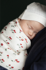 Newborn baby swaddled in a strawberry patterned blanket with a white hat on a dark background