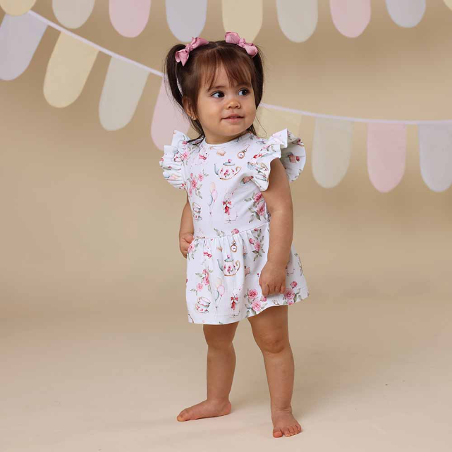 Young child wearing a floral dress standing in front of a decorative banner.