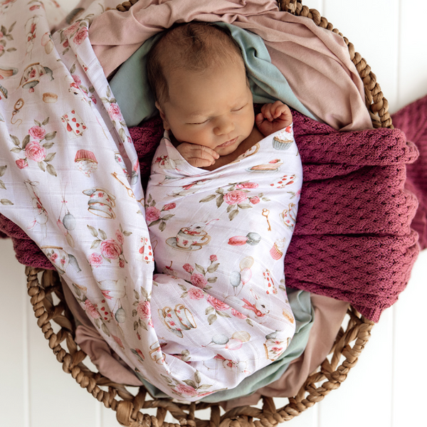Newborn baby swaddled in a floral blanket in a woven basket.
