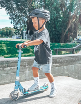 Child riding a scooter with a helmet on a sunny day outdoors.
