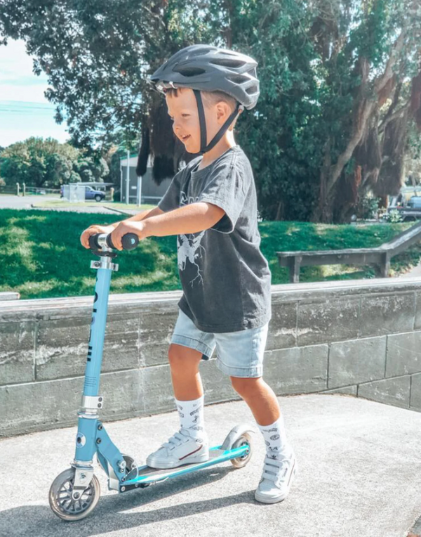Child riding a scooter with a helmet on a sunny day outdoors.