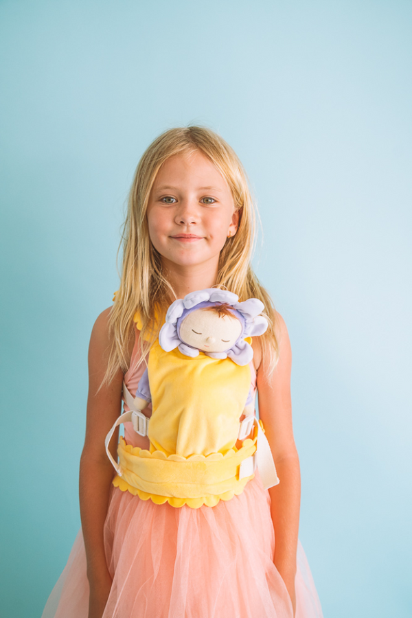 Child wearing the OLLI ELLA Dinkum Dolls Petal Carrier - Buttercup with Lavender doll