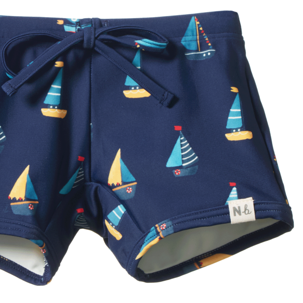 Detail view of navy blue swim shorts with sailboat pattern on a white background