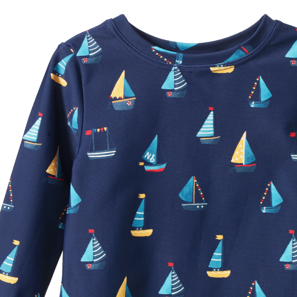 Detail view of navy blue long-sleeve swim top with colourful sailboat pattern on a white background
