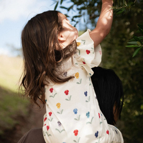 Child in a floral romper reaching up to a tree outdoors