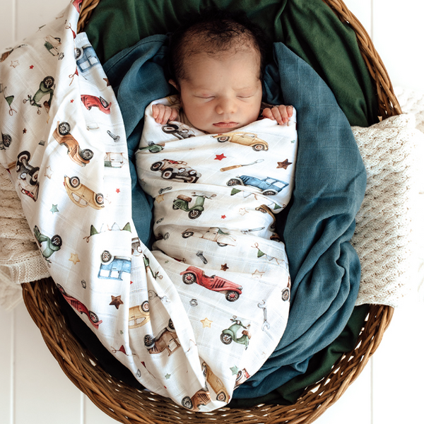 Newborn baby wrapped in a blanket with vehicle pattern, lying in a woven basket.