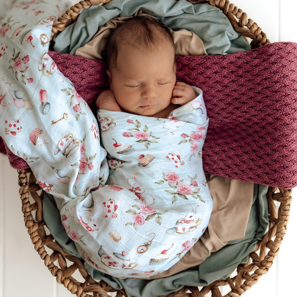 Newborn baby wrapped in a floral blanket in a wicker basket with soft textures