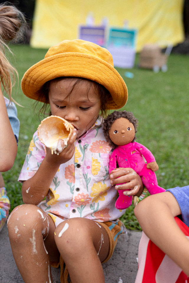 Child eating ice-cream while holding OLLI ELLA Dinky Dinkum Doll Sadie Sprinkles