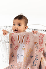 Baby sitting in bassinet with INDUS DESIGN Nature Bunny Blanket hanging over the side close up