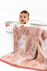 Baby sitting in bassinet with INDUS DESIGN Nature Bunny Blanket hanging over the side 