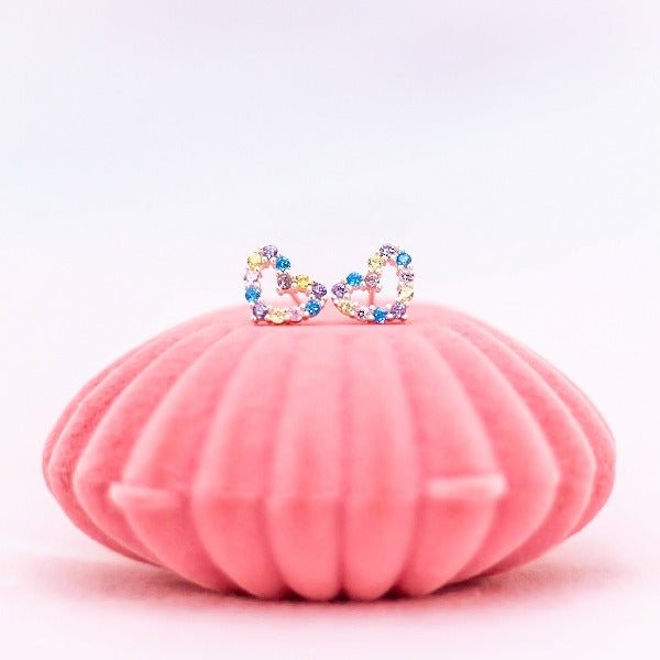 LAUREN HINKLEY Gem Heart Earrings sitting on top of pink shell case