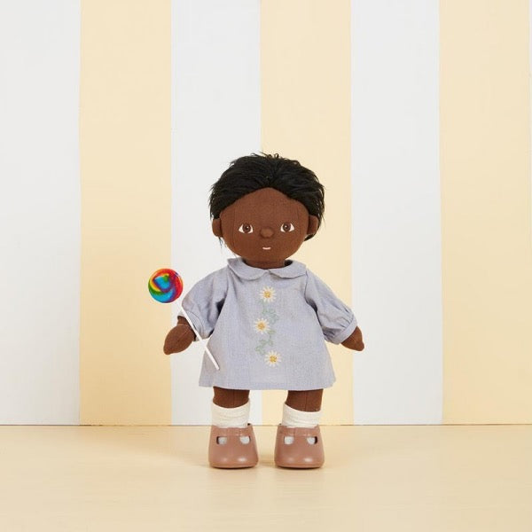 Tiny wearing the OLLI ELLA Dinkum Doll Cotton Daisy Dress and holding a lollipop